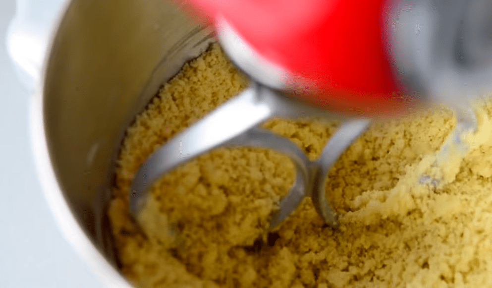 Stand-mixer paddle working flour, sugar, and butter into fine golden crumbs