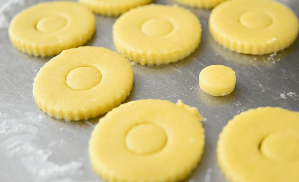 Unbaked scalloped cookies with small circular cutouts alongside them on a metal baking sheet
