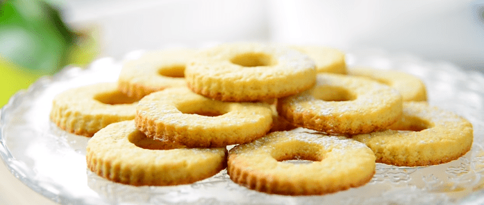 Baked ring-shaped lemon shortbread cookies dusted with powdered sugar on a glass plate