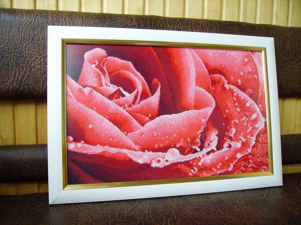 Framed cross-stitch of dew-covered pink and red roses resting against a brown leather sofa