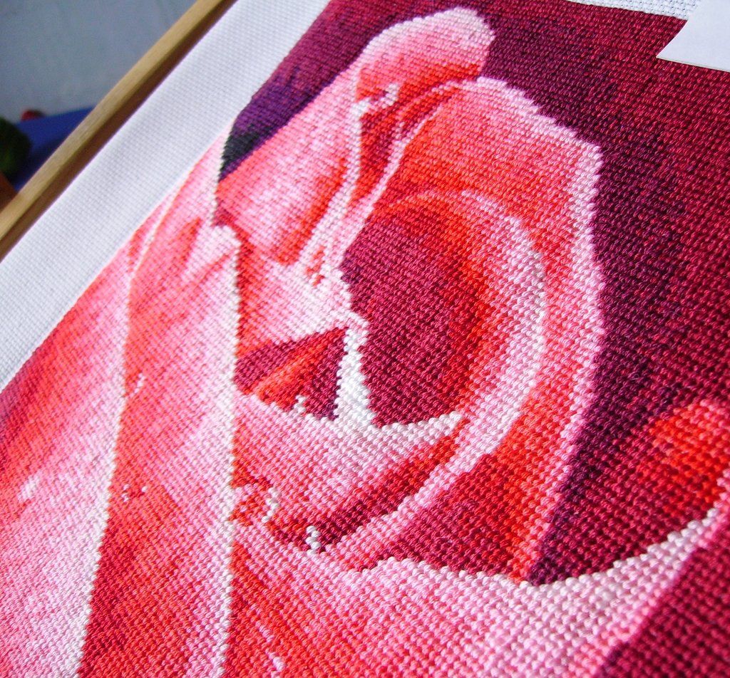 Macro view of individual cross-stitches forming pink rose petals on burgundy and white fabric