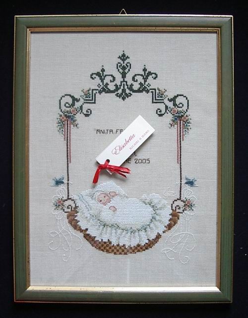 Framed cross-stitch birth sampler with a sleeping baby in a cradle