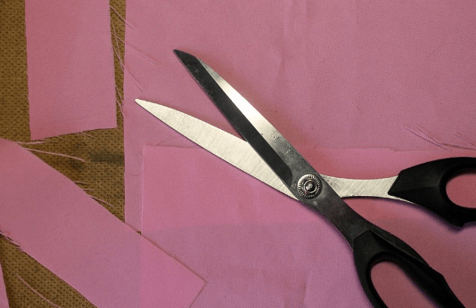 Scissors on pink fabric for cutting out a bow tie