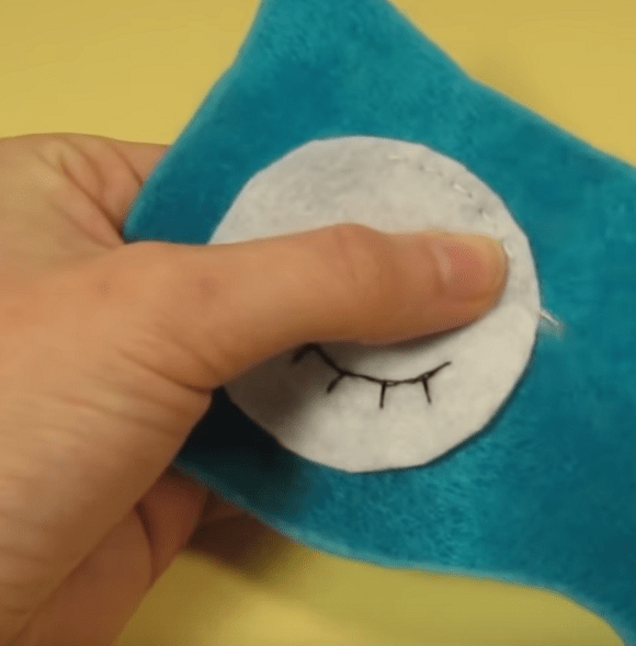 Sewing the white eye piece onto the blue felt mask base
