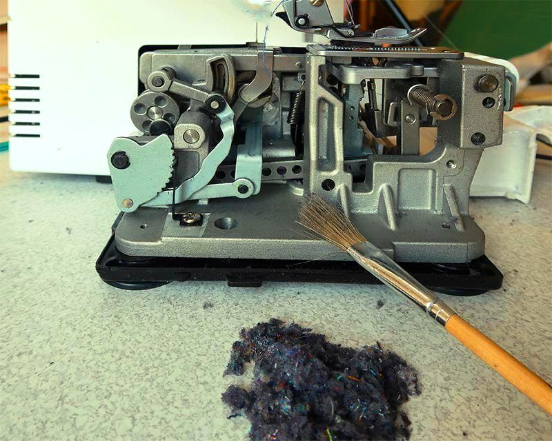 Open serger with a cleaning brush and lint on the table