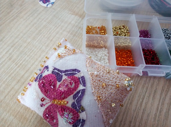 Embellishing the butterfly with beads on a fabric pincushion