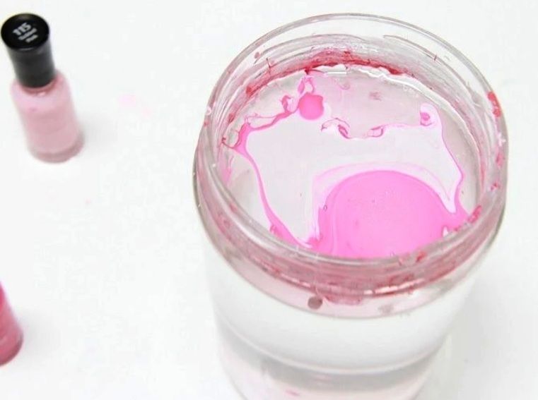 Small decorative object being dipped into water for a nail-polish marbling finish