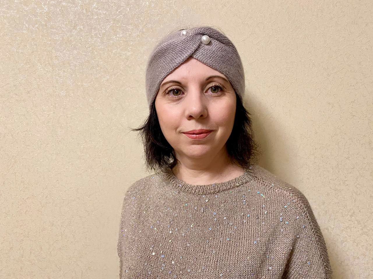 Женщина в серой вязаной повязке-чалме и бежевом джемпере с пайетками, портрет вполоборота