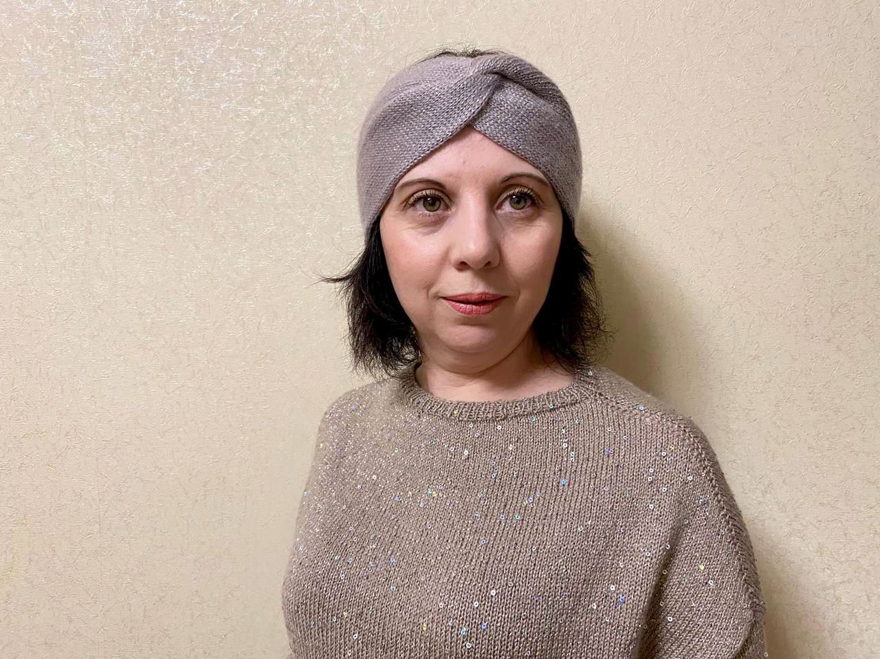 Женщина в серой вязаной повязке-чалме и бежевом джемпере на светлом фоне