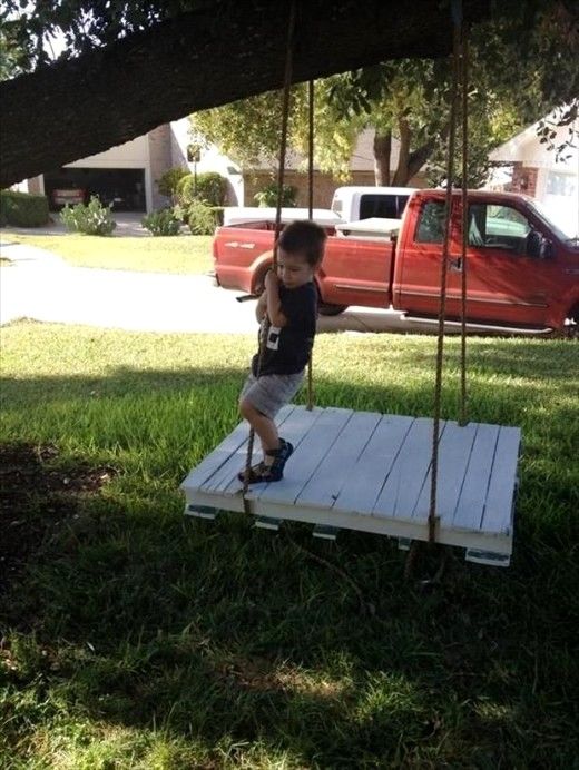 Child standing on a suspended wooden pallet platform swing in a yard