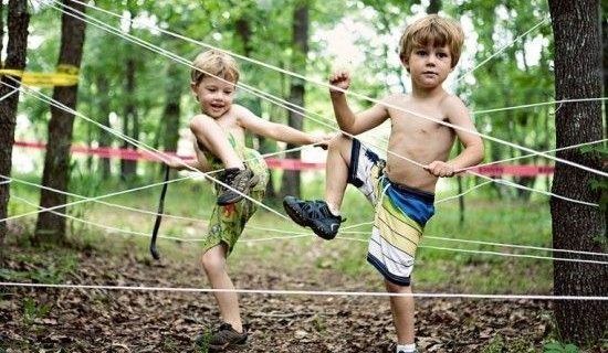 Two children moving through a rope obstacle course strung between trees