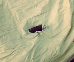 Close-up of a ragged tear in pale green tent rainfly fabric.