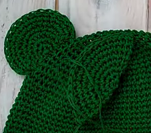 Sewing a green eye onto the top of the frog hat