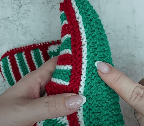 Green sole and heel of the Christmas slipper on knitting needles