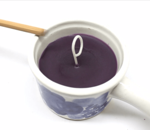 Looped white cotton wick centered in a ceramic cup filled with purple wax