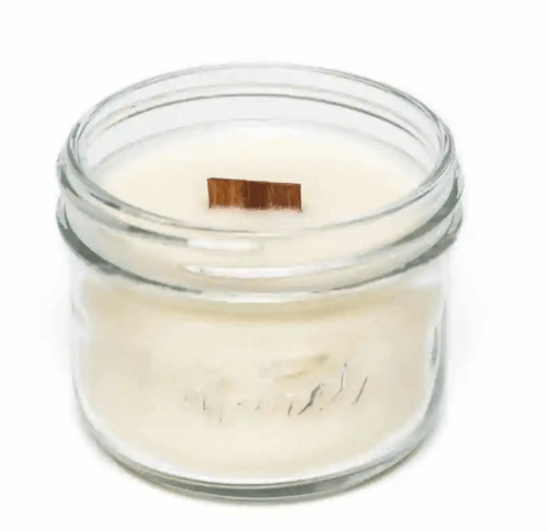 Small clear glass candle jar filled with white wax and a short rectangular wooden wick