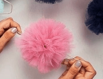 Hands fluffing a finished pink tulle pom-pom