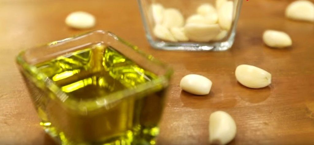 Очищенные зубчики чеснока рядом с небольшой стеклянной ёмкостью оливкового масла