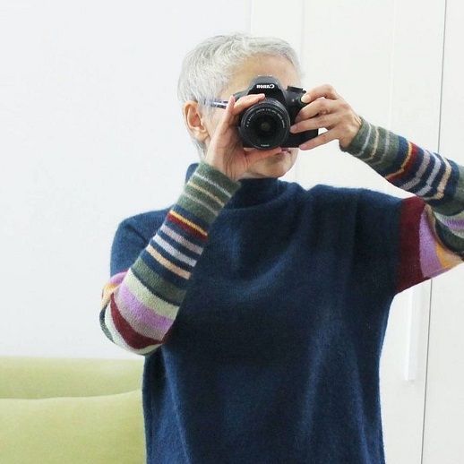 Темный свитер с полосатыми рукавами на женщине с фотоаппаратом