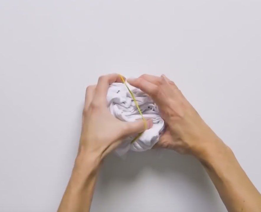 Hands tightening rubber bands around a twisted T-shirt