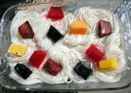 Damp yarn strands arranged in a glass container with colorful ice cubes on top