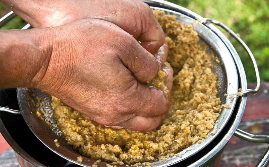 Руки отжимают измельчённую яблочную мякоть над дуршлагом