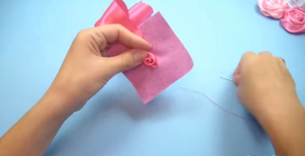 Satin ribbon rose center being sewn to a felt base