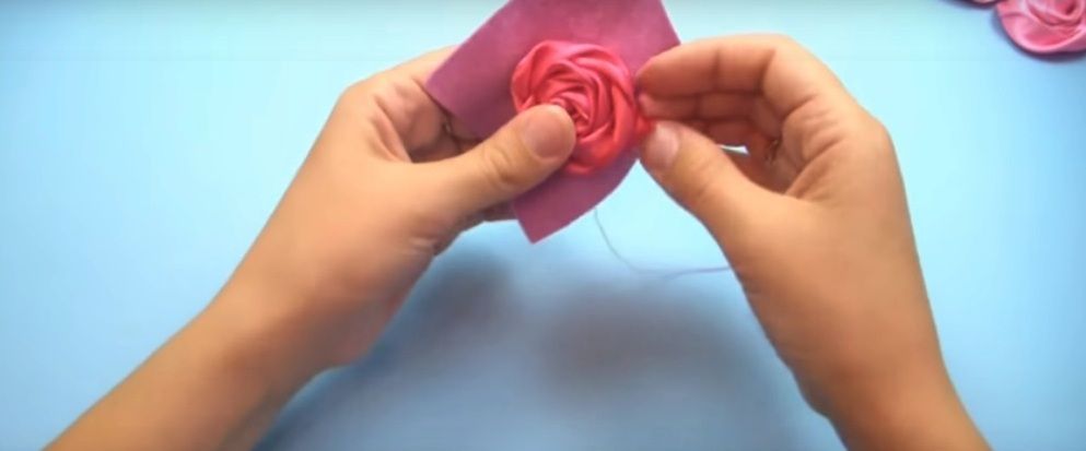 Securing an outer petal on the satin ribbon rose