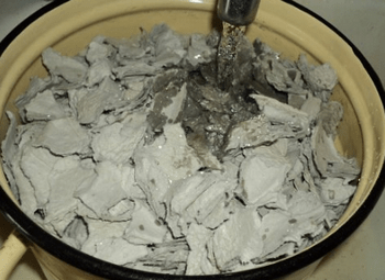 Кусочки мокрой серой бумажной массы в большой эмалированной кастрюле