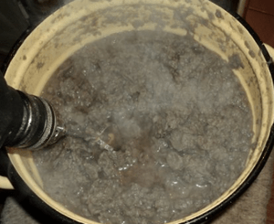 Electric drill mixer blending grey paper pulp in a large pot