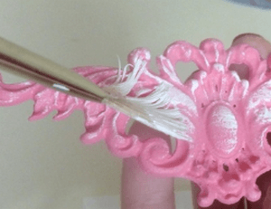 White paint being applied over a pink decor piece