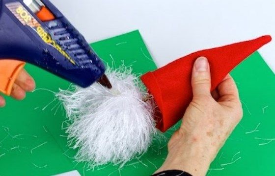 Gluing the white beard to the elf's red hat using hot glue