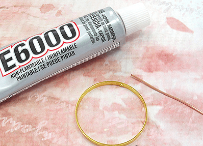 Tube of glue, a gold-tone hoop, and thin wire for an earring