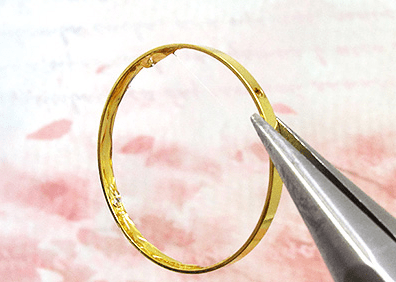 Needle-nose pliers holding a gold-tone hoop earring base
