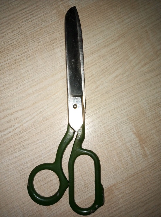 Large metal dressmaking shears with dark-green handles resting on a light wood-grain surface