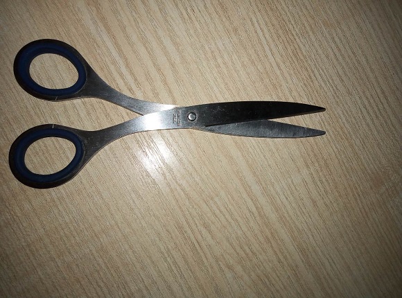 Small black-handled scissors with short pointed blades on a light wood-grain surface