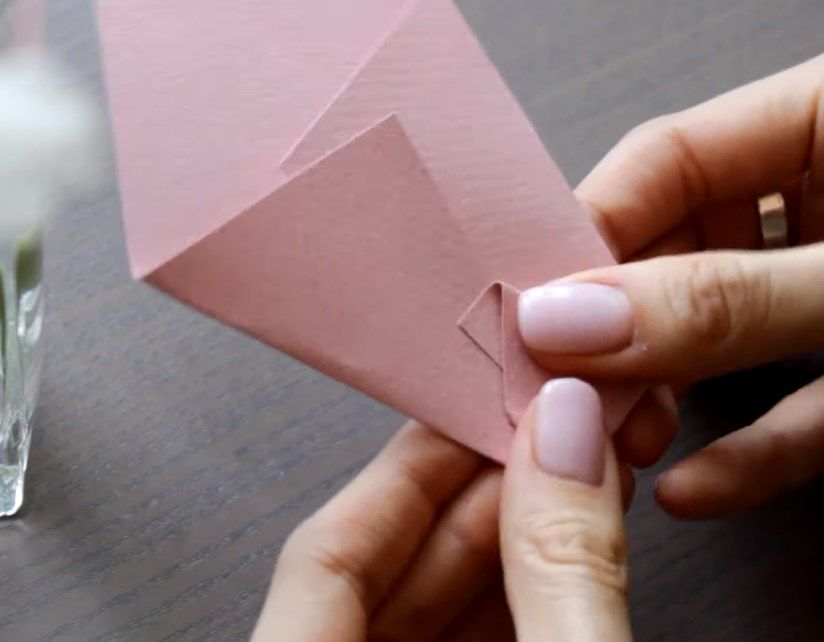 Hands folding a pink paper envelope