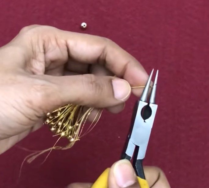 Using round-nose pliers to form a loop on the pin above the tassel
