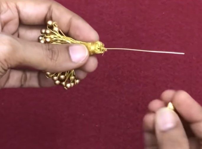 Sliding an end cap and a large bead onto the pin above the tassel