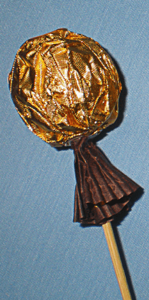 Round candy on a wooden skewer in gold wrapping