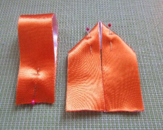 Orange ribbon bow piece with a center crease and pins