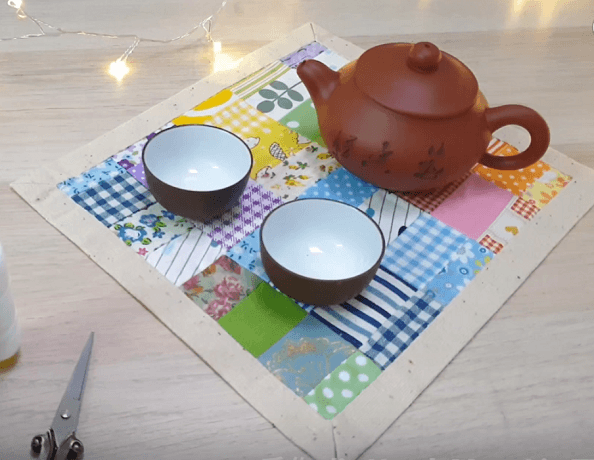 A teapot and two bowls on a square patchwork napkin