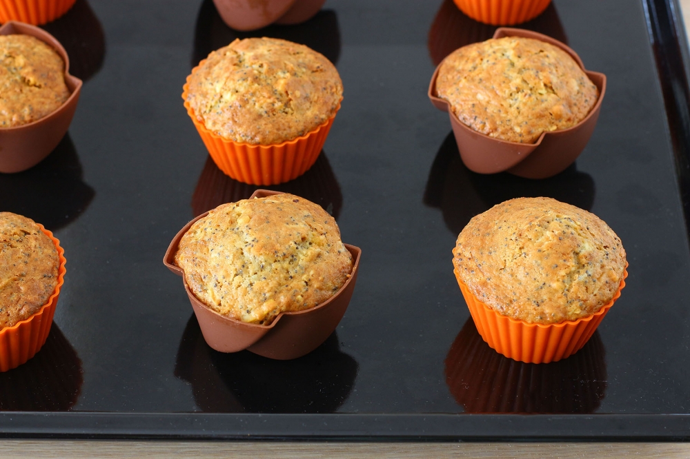 Golden apple and poppy-seed muffins baked in orange and brown silicone molds on a black tray